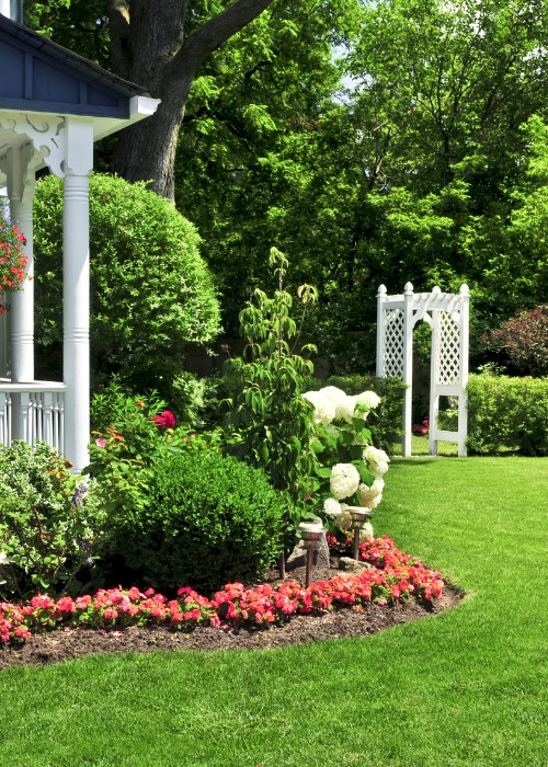 Well-maintained home garden with manicured trees, shrubs, and flower beds.