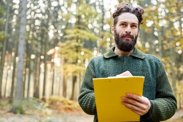 Certified arborist holding clipboard during forest tree assessment.
